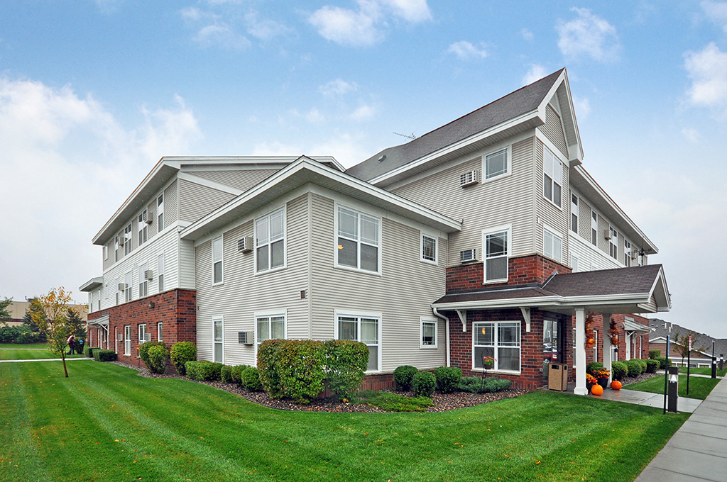 a large apartment building with green grass and a sidewalk